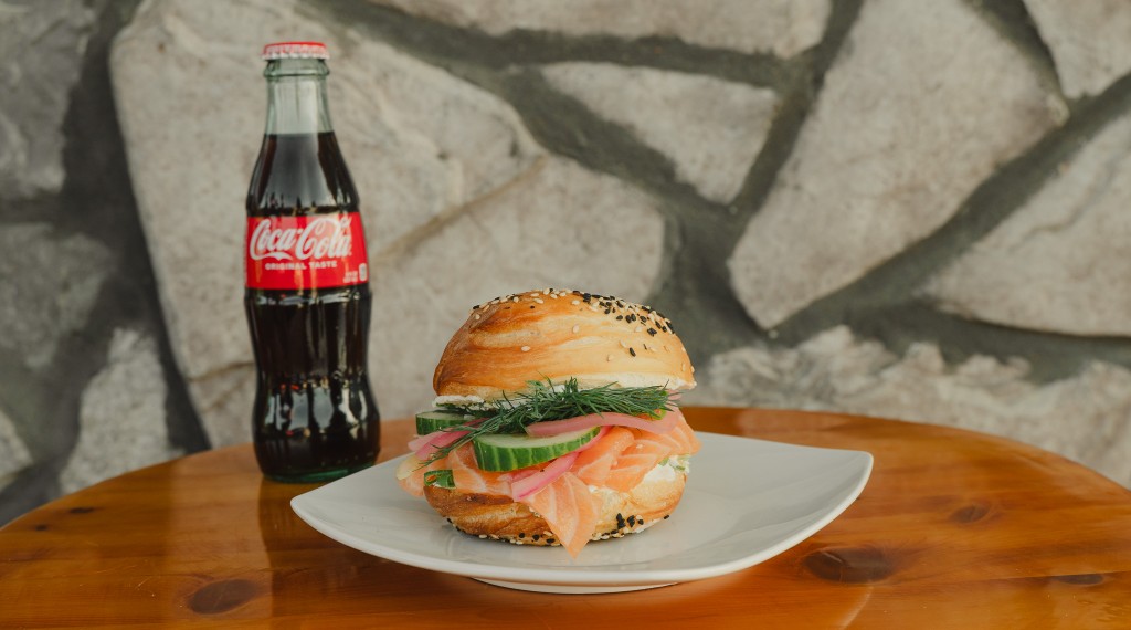 Everything bagel sandwich with lox, cucumber, and dill on a white plate
